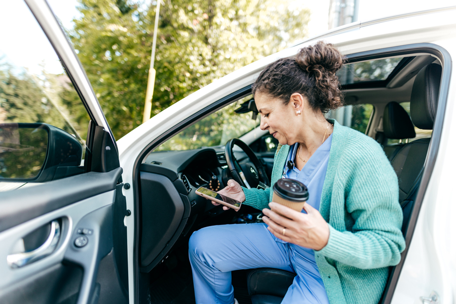 Woman in scrubs looking at phone and getting out of car